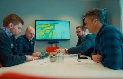 Fire personer rundt et møtebord med et kart over et boligområde på skjermen i bakgrunnen