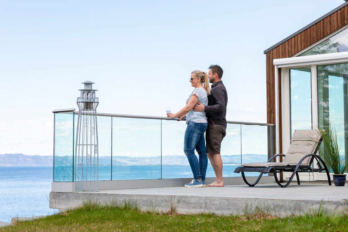 Mann og kvinne ser ut over sjøen fra terrasse på moderne funkishus