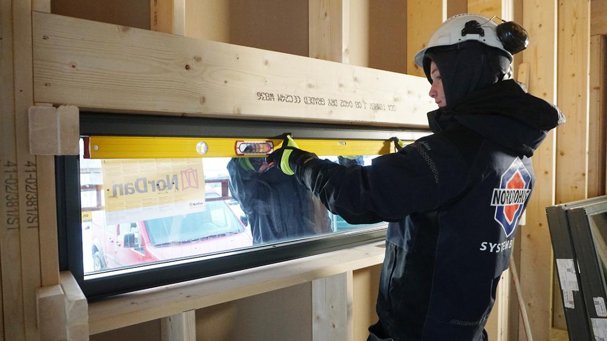 Tømrerlærling Erlend Åsen bruker vater for å sjekke at et vindu er riktig plassert i veggen.