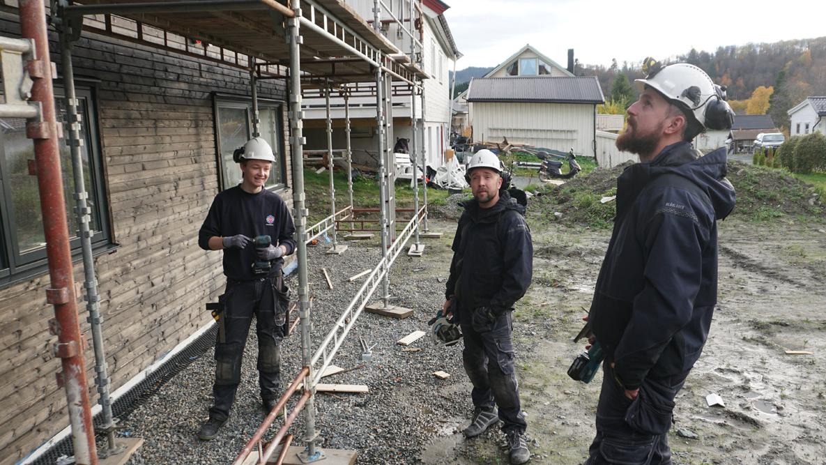 Tre tømrere foran en enebolig fra Nordbohus med stilas