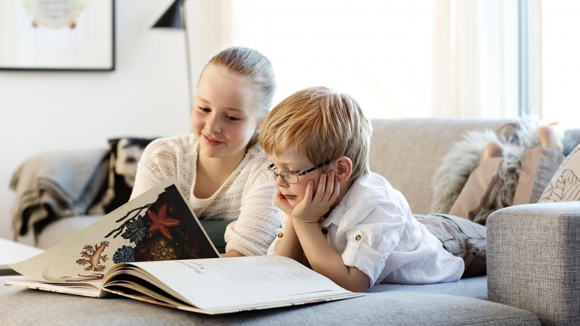Miljøbilde som viser en gutt og en jente som leser bok i en sofa