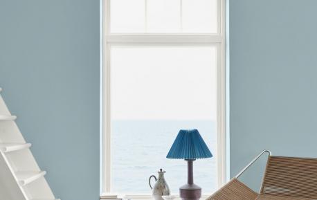 Et rom med blå vegg. et vindu med en lampe og en hvit trapp til venstre