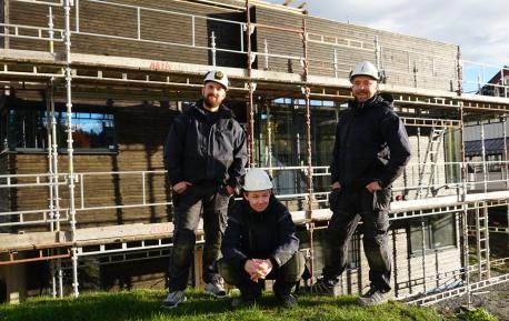 Tre tømrere foran en enebolig fra Nordbohus med stilas