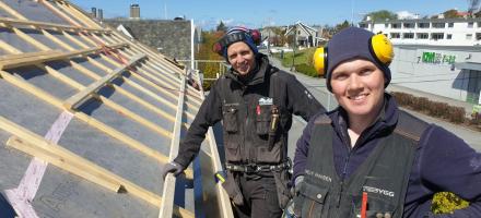 To blide arbeidere fra Nordbohus TG Bygg som monterer tak og smiler til kamera.